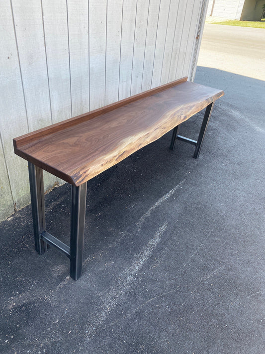 iReclaimed black walnut live edge sofa bar table with steel legs. Natural finish highlights wood grain. Customisable height and edge style.